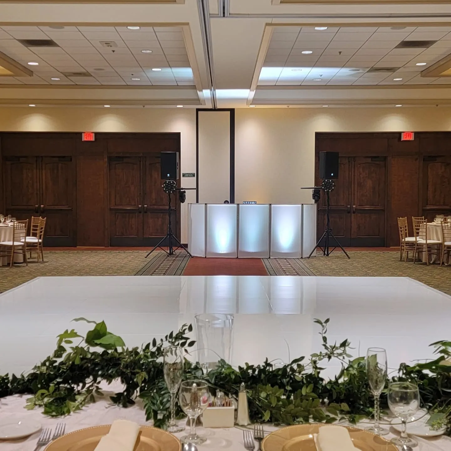 White dance floor and DJ setup in a greenery-dressed ballroom